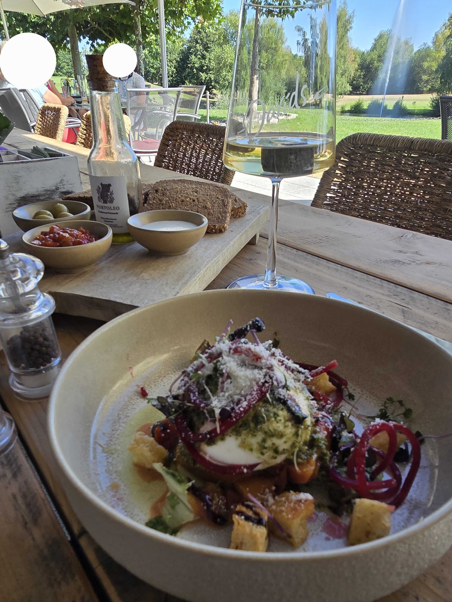 Salat mit Mozzarella und Rote Bete, daneben Brot und ein Glas Weißwein mit Blick auf den Golfplatz